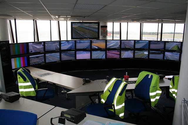 Control room with multiple CCTV monitors displaying surveillance feeds, equipped with desks, chairs, and high-visibility jackets, emphasizing 24/7 security monitoring services.