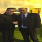 Two men shaking hands, one in a black suit and the other in a black shirt, representing close protection services and client relationship in a professional setting.